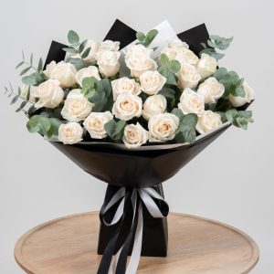 Buchet surpriză cu trandafiri albi, bujori și eucalypt, înfășurat în hârtie albă și panglică satinată, livrat la domiciliu în Focșani.